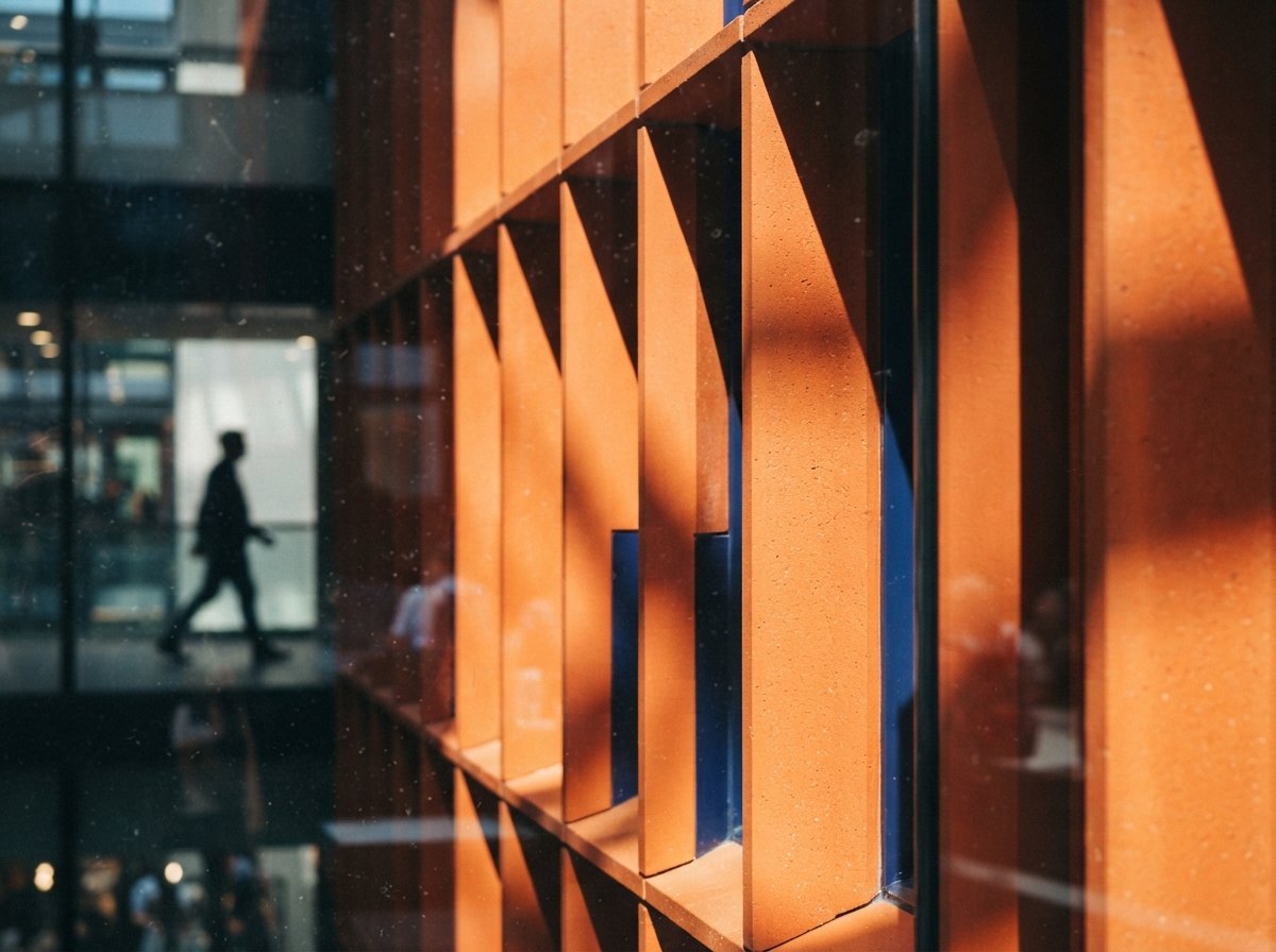 A close-up shot of an orange terracotta facade casting diagonal shadows with a glass glare in the foreground.