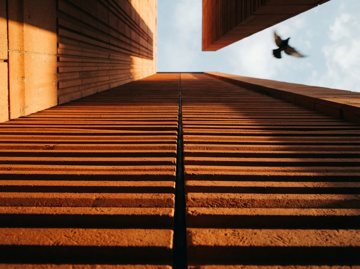 A close-up worm's-eye view of a ribbed terracotta facade catching raking golden morning light.