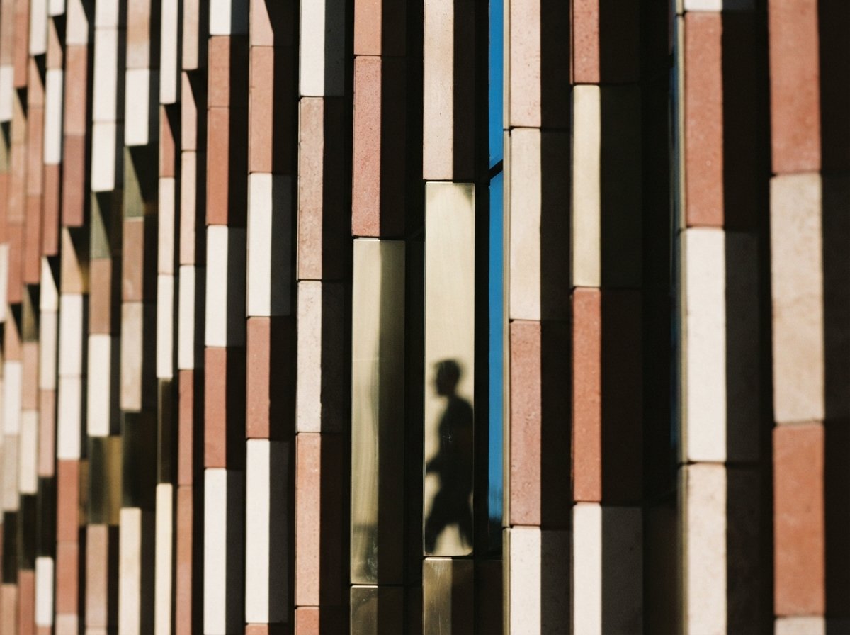 A close-up view of geometric terracotta and brass building louvers throwing crisp diagonal shadows under intense sunlight.
